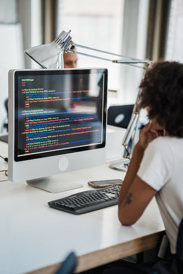 A female professional focused on coding at her office desk with a desktop computer.