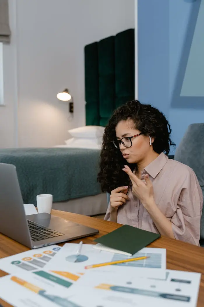 home-hero Woman working from home on a video call using a laptop, sitting at a desk in a modern bedroom.
